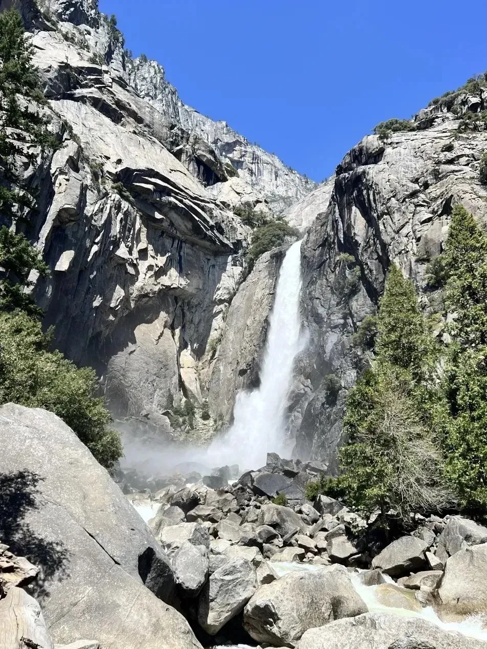 A waterfall in Yosemite pouring between granite cliffs into a field of boulders under a deep blue sky.