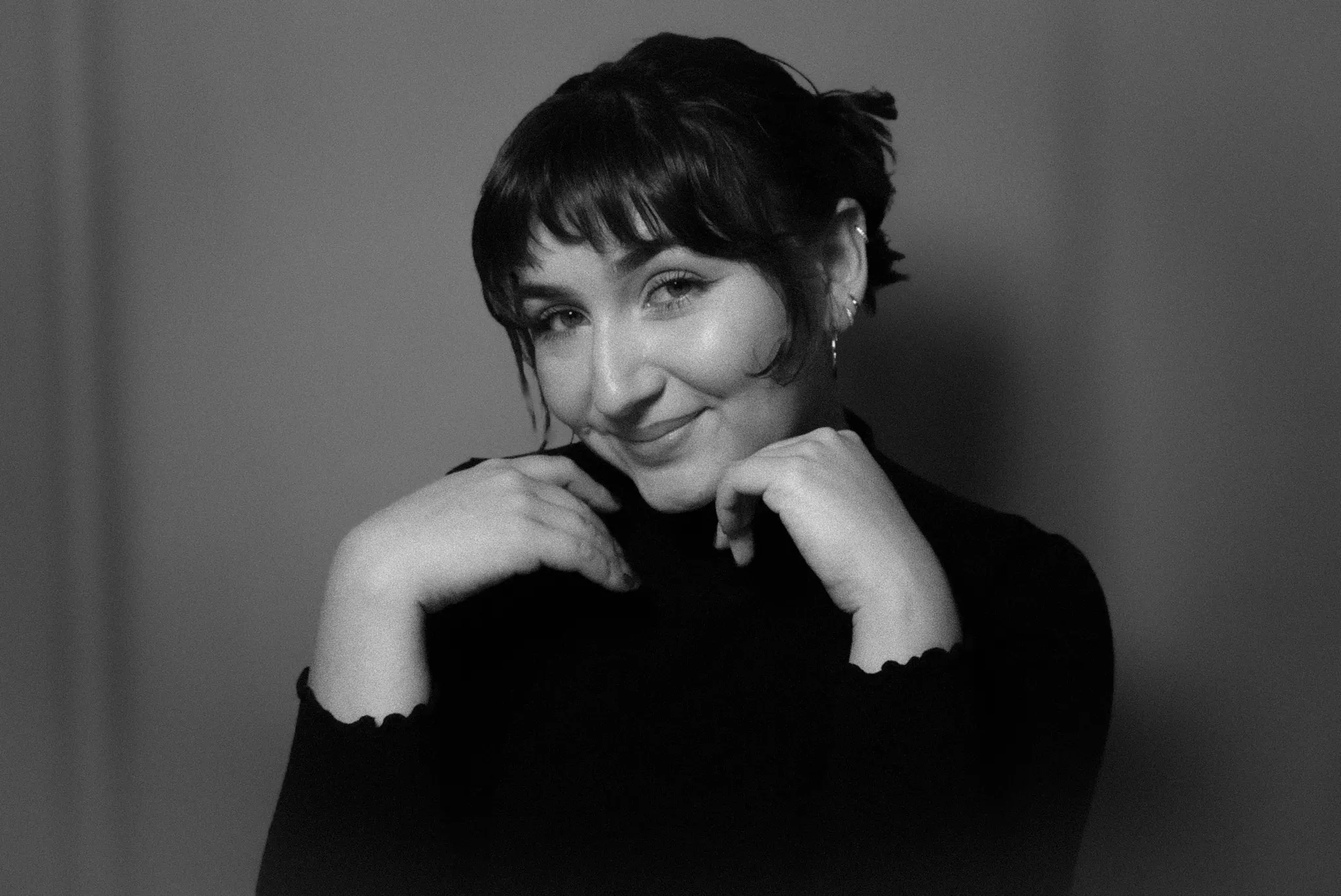 A black-and-white portrait of Alyssa smiling with her head tilted and her hands near her chin.